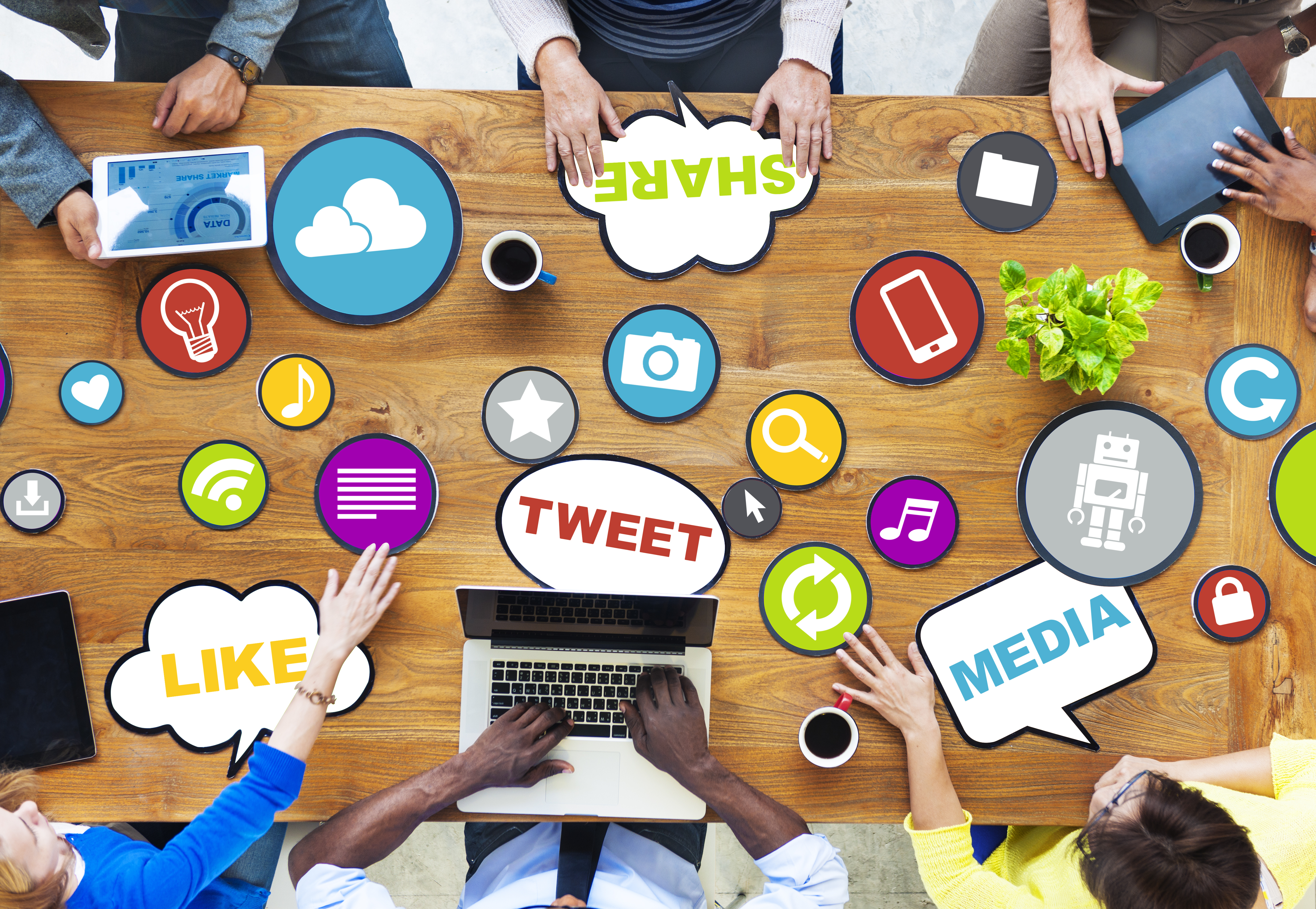 group of people sitting at a table,with emojis and icons on it,working on their devices 